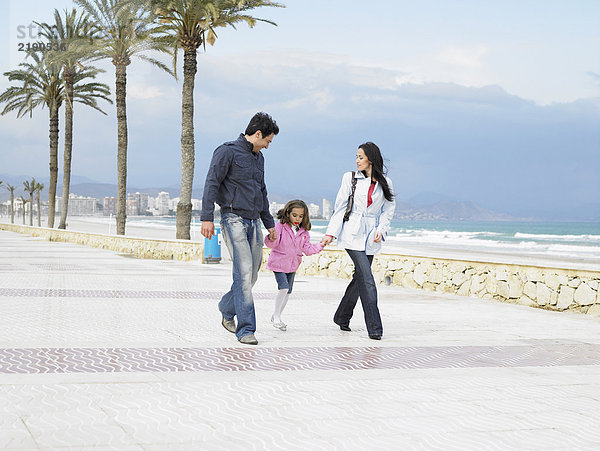 Mutter und Vater gehen mit ihrer kleinen Tochter (6-8) am Meer entlang. Alicante  Spanien.