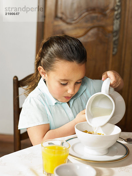 Mädchen (4-6) beim Frühstück Milch auf Müsli gießen
