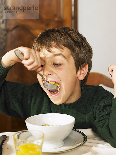 Junge (6-8) beim Frühstück Müsli essen