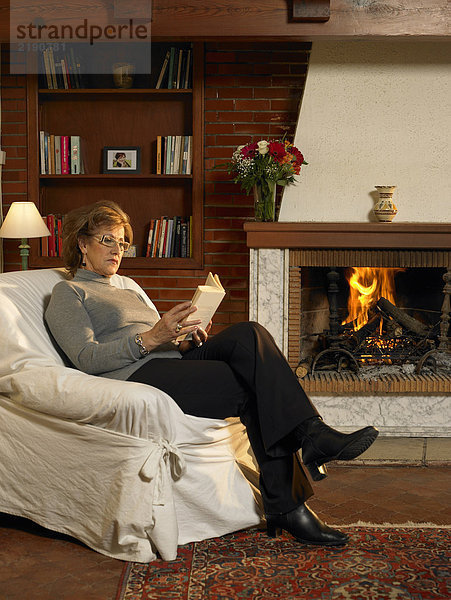 Seniorin liest Buch bei Feuer im Wohnzimmer