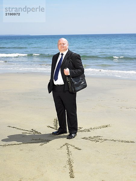 Mann am Strand mit Pfeilen im Sand um ihn herum.