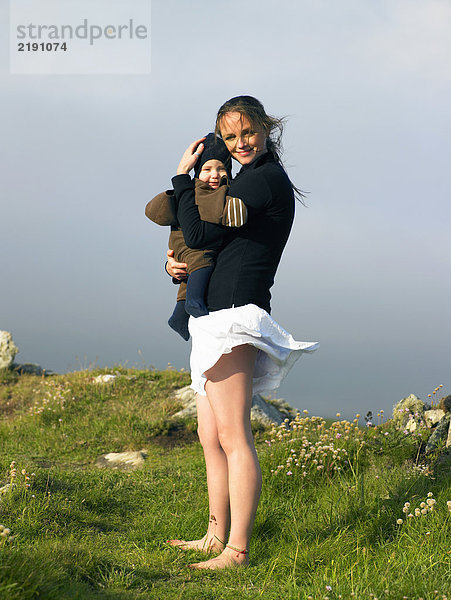 Junge Frau hält Baby mit dem Wind  der ihren Rock bläst.