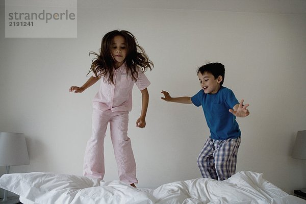 Mädchen und Junge springen auf einem Bett.