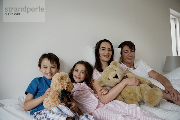 Porträt einer Familie  die auf einem Bett sitzt.