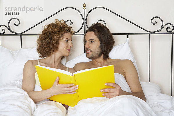 junges Paar im Bett mit gelbem Buch