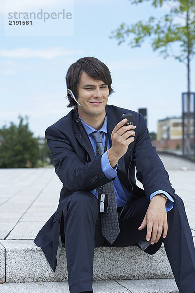 Geschäftsmann sitzt auf einer Treppe mit Kopfhörer und schaut auf sein Handy.