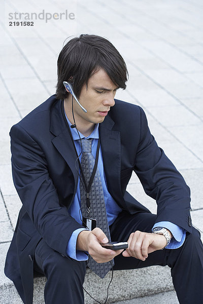 Geschäftsmann sitzt auf einer Treppe und schaut auf seine Uhr mit Headset und Handy.