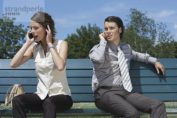 Geschäftsmann und Frauen sprechen auf dem Handy  während sie draußen auf der Bank sitzen.