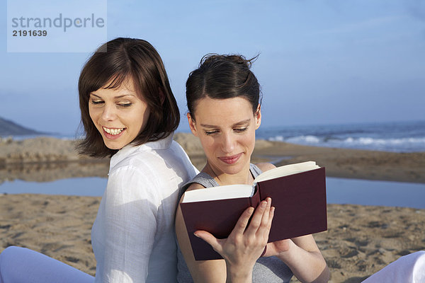 zwei Frauen sitzen zusammen am Strand und lesen