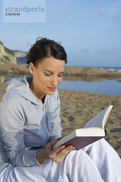 Junge Frau am Strand Porträt lesen ein Buch Meer und Himmel im Hintergrund.