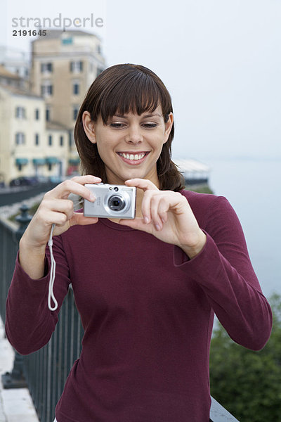 Porträt einer jungen Frau mit Kamera  die im Hintergrund eine lächelnde Altstadt fotografiert.