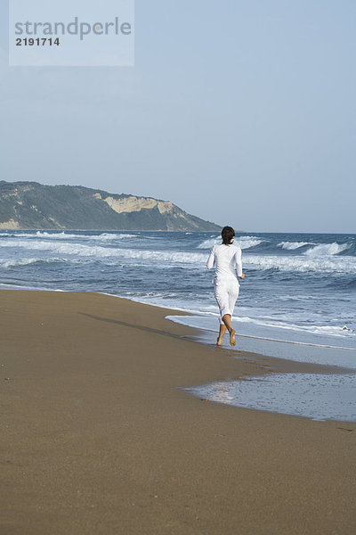 Frau joggt vor der Kamera am Strand.