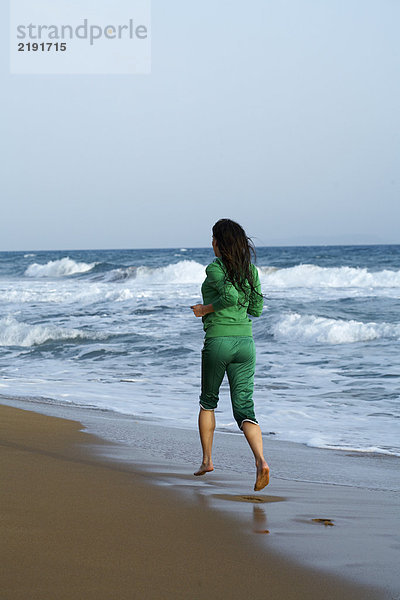 Frau  die am Strand vor der Kamera joggt.