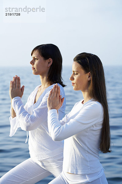 Zwei junge Frauen beim Yoga am Meer.