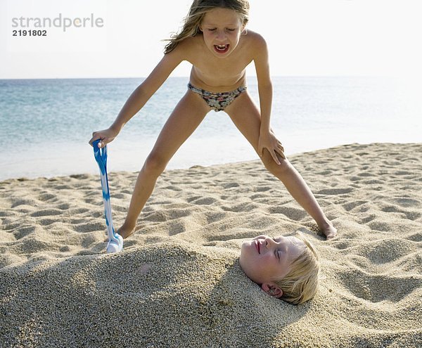 Junges Mädchen begräbt kleinen Jungen im Sand am Strand .