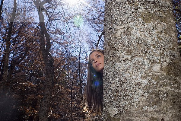 Junge Frau  die sich hinter einem Baum versteckt.