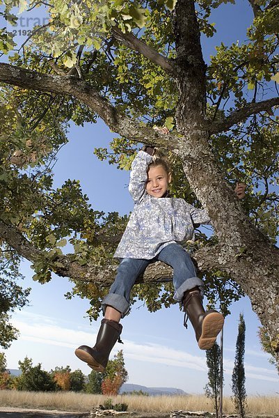 Ein junges Mädchen  das lächelnd auf einen Baum klettert.
