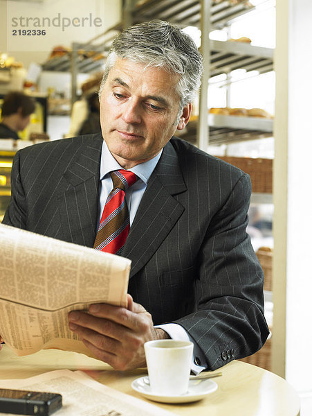 Der reife Geschäftsmann sitzt im Café und liest die Finanzzeitung.