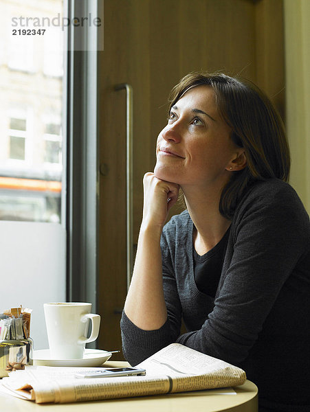 Frau im Café sitzend  Kinn auf der Hand liegend  lächelnd