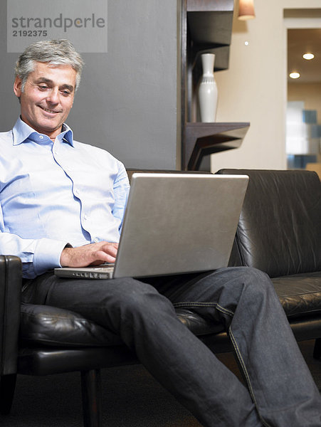 Reifer Mann auf dem Sofa sitzend mit Laptop  lächelnd