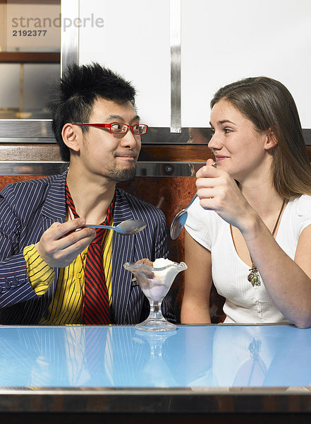 Junges Paar teilt sich Eis im Café und lächelt sich an.