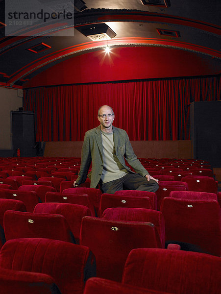 Reifer Mann im leeren Kino sitzend  lächelnd  Portrait