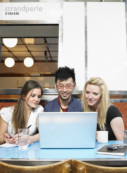 Drei Leute  die einen Laptop in einem Diner anschauen.