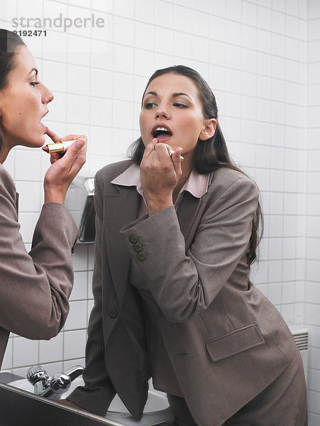 Frau spiegelt sich im Büro-Waschraumspiegel mit Make-up