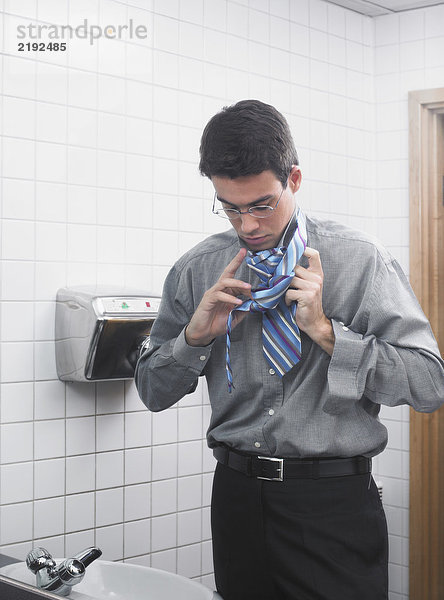 Mann spiegelt sich im Waschraumspiegel  der seine Krawatte hochzieht.