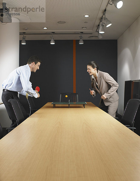 Mann und Frau spielen Miniatur-Pingpong am Konferenztisch