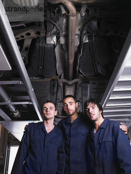 Drei Mechaniker stehen unter einem angehobenen Wagen.