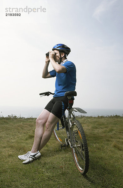 Ein männlicher Radfahrer schaut durch ein Fernglas.