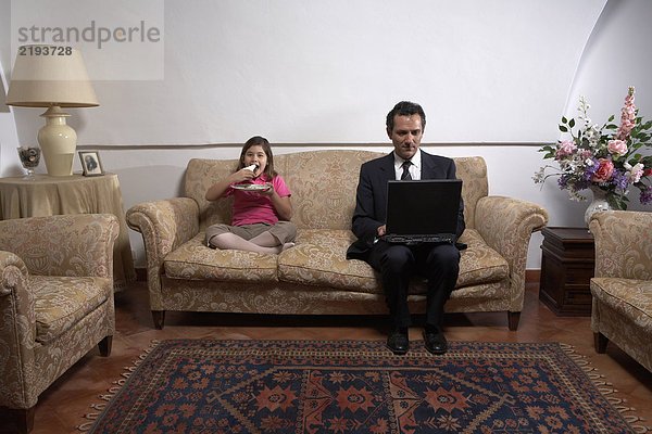 Mann mit Laptop und Tochter (6-8) auf dem Sofa beim Kuchenessen