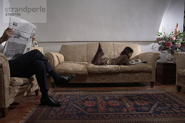 Mann liest Zeitung mit Tochter (5-7) Lesebuch auf Sofa