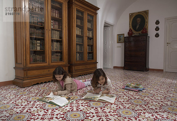 Mädchen (6-11) liegen auf dem Boden und lesen Bücher.