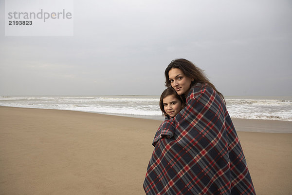 Mutter und Tochter (9-11) in Decke gewickelt am Strand