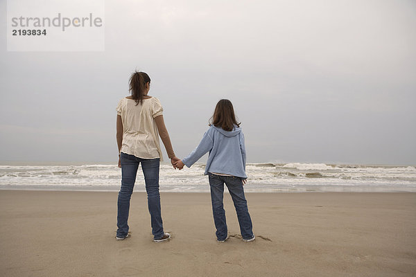 Mutter und Tochter (9-11) beim Händchenhalten am Strand  Rückansicht