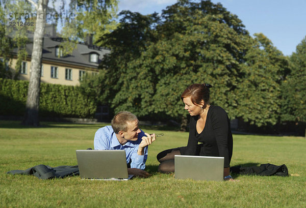 Mann und Geschäftsfrau sitzen im Park mit Laptop