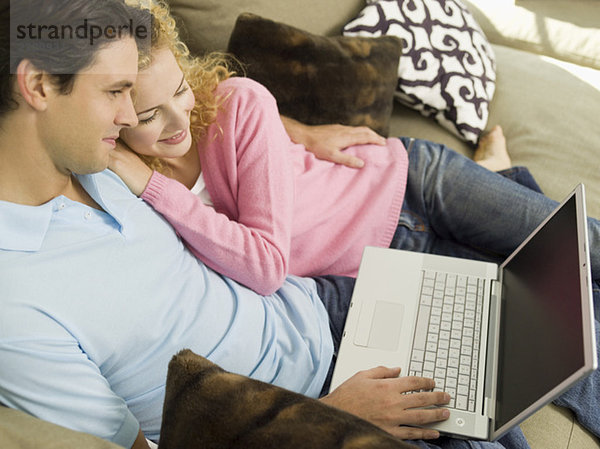 Junges Paar auf Sofa  Mann mit Laptop  lächelnd  Portrait