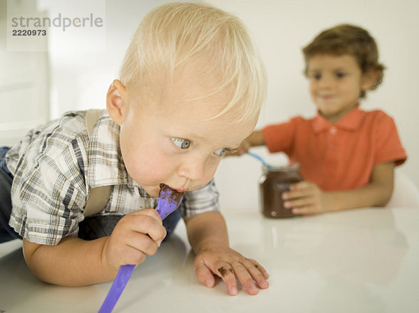 Zwei Jungen (4-5)  (12-24 Monate)  Junge leckt Schokolade vom Löffel  Porträt