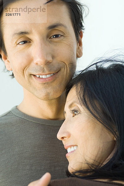 Mann lächelt in die Kamera  während die Frau ihren Kopf auf seine Brust lehnt.