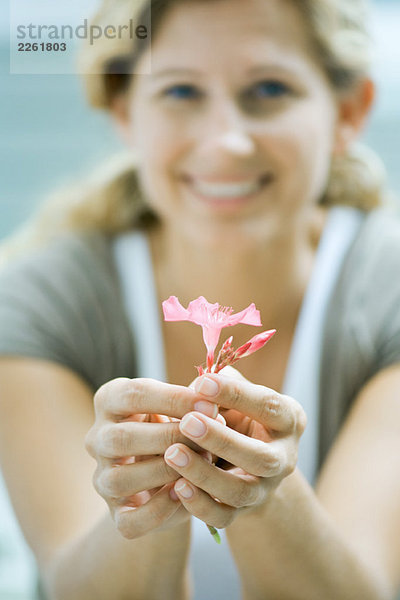 Frau hält Blume in den Händen  lächelt in die Kamera  fokussiert auf den Vordergrund