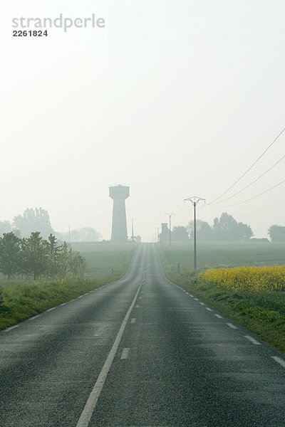 Straßen- und Telefonleitungen in nebliger Landschaft  Wasserturm in der Ferne