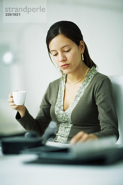 Frau am Schreibtisch sitzend  Kaffeetasse haltend  nach unten schauend
