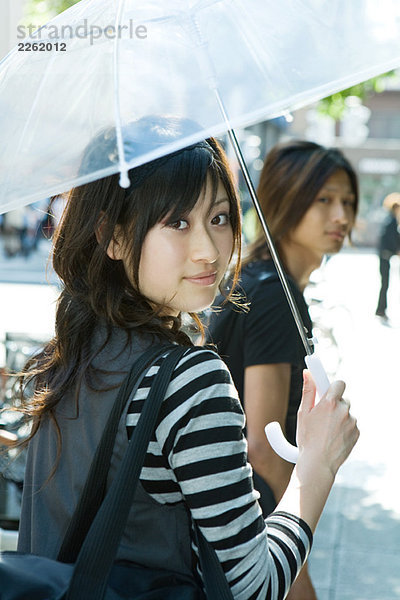 Junge Frau mit Sonnenschirm  lächelnd über die Schulter vor der Kamera