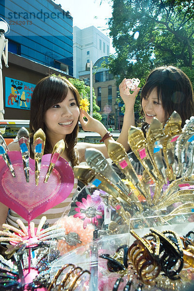 Zwei junge Frauen auf dem Straßenmarkt  probieren Haarschmuck an  lächeln