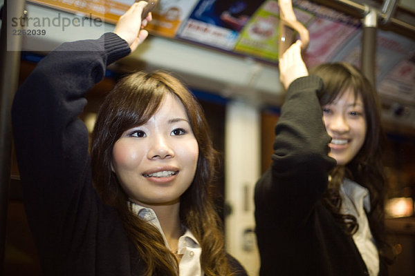 Zwei junge Frauen stehen in der U-Bahn  die Arme erhoben  lächelnd