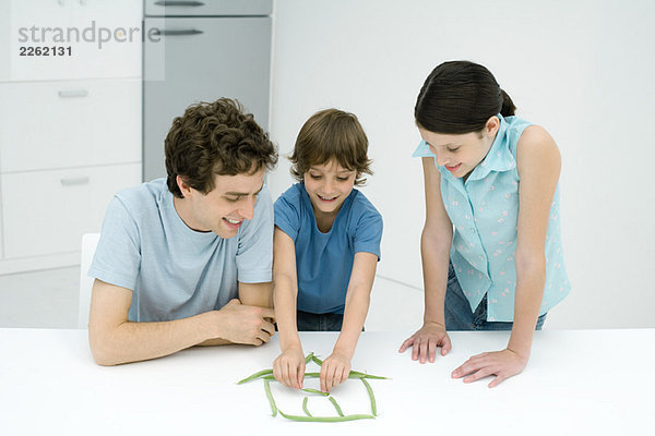 Kleiner Junge in der Küche mit Vater und Schwester  Hausbau aus grünen Bohnen  alle lächelnd