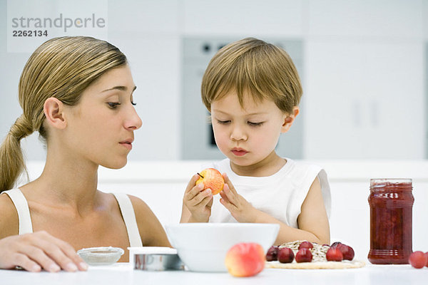 Mutter und Sohn kochen gemeinsam  Junge hält Apfel  beide schauen nach unten