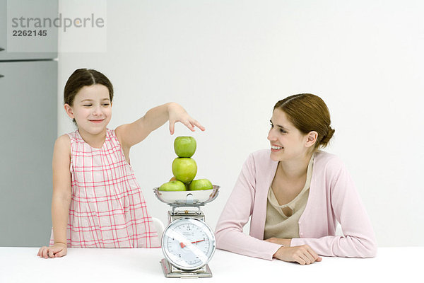 Mutter und Tochter stapeln Äpfel  beide lächelnd.